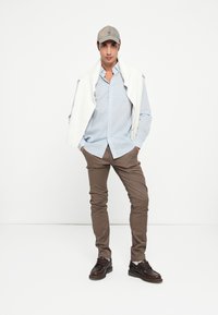 Vaaleansininen napitettava paita, valkoinen neule yllä, ruskeat slim-fit-housut ja tummanruskeat nauhakenkä.