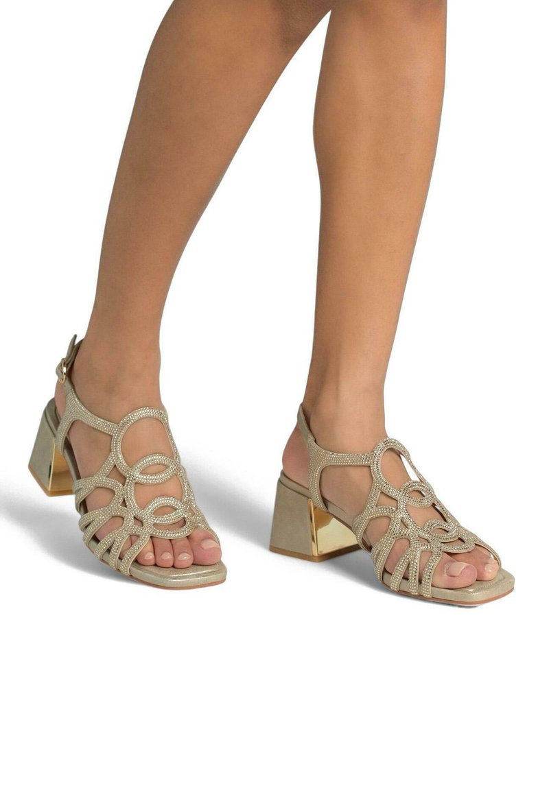 Goldfarbene Sandalen mit Blockabsatz, die ein geflochtenes Riemendesign mit Verzierungen, eine offene Zehenpartie und einen hinteren Knöchelriemen zur Unterstützung aufweisen.