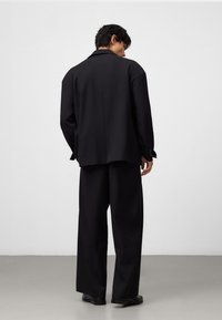 Svart överdimensionerad kostymjacka och vida byxor i ett mjukt material. Har en enkel slits, notch-krage och minimalistisk design.