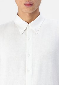 Witte linnen shirt met een button-down kraag, met een gestructureerde stof en kleine witte knopen langs de voorplacket.