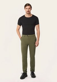 Black fitted t-shirt, olive green tailored pants with a button closure, and black lace-up shoes, against a neutral background.