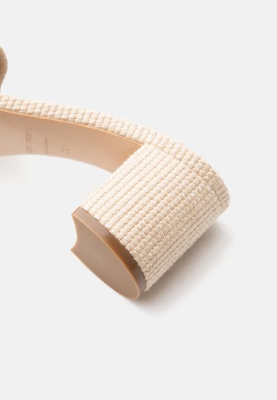 Μπεζ πλεκτό τακούνι με καμπυλωμένη καφέ σόλα από καουτσούκ, μέρος ενός κλειστού παπουτσιού γυναικείας συλλογής που παρουσιάζεται σε λευκό φόντο.