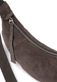 Brun mockakvadrat med en böjd form, med dragkedjestängning, en rem och en texturerad yta. Accenter inkluderar läderdetaljer.