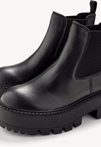 Botas de tobillo de cuero negro con costados de malla texturizada, puntera redondeada, suela de plataforma gruesa y un dibujo distintivo para tracción.