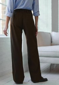 Bruine, wijde broek gemaakt van textuurstof, met een elastische tailleband en achterzakken, gedragen met een lichtblauw shirt.
