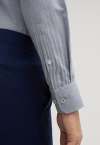 Hemd mit kariertem grauen Muster, weißen Knopfmanschetten und passenden navyblauen Hosen. Baumwollmaterial mit glatter Textur.