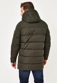 Dunkelgrüne Steppjacke mit Kapuze, die ein gestepptes Design und elastische Bündchen aufweist, von hinten sichtbar mit einer glatten Textur.