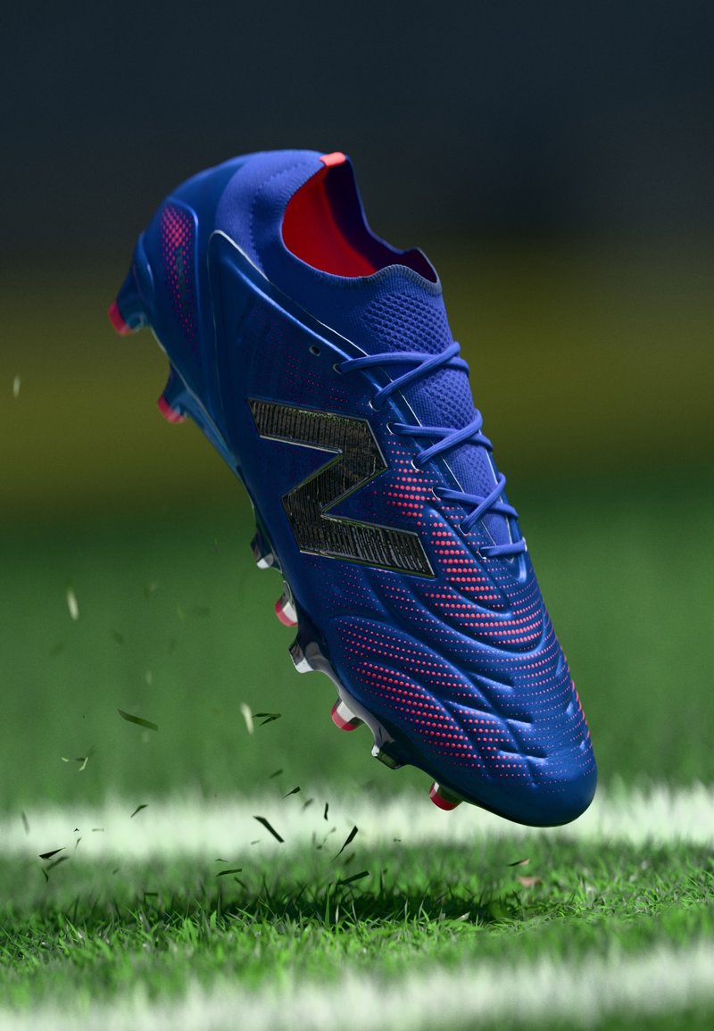 Μπλε ποδοσφαιρικό παπούτσι με υφή, με μαύρο λογότυπο, φωτεινές κόκκινες λεπτομέρειες και ενισχυμένη σόλα με λευκές και ροζ επικαθίσεις.
