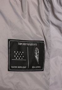 Grå nyloninredning med en svart etikett som har vit text och ikoner för "Vattentålig" och "Äkta Dun."