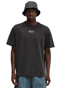 Sort bomulds-t-shirt med et lille hvidt logo på brystet og korte ærmer, parret med en mørkeblå bøttehat.