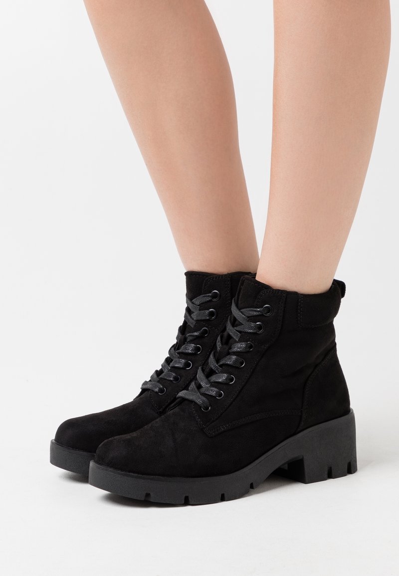 Zwarte enkellaarsjes van suède met een vetersluiting aan de voorkant, stevige rubberen zolen en versterkte zijkanten. Voorzien van grijze veters en een strak design.