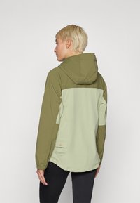 Grønn og lys grønn hettejakke med buet hem, med en lomme med knappdetalj på baksiden. Lett, utendørs design.