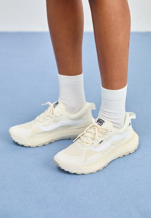 Kreemivärvi Vans tennisjalatsid valgete aksentidega, millel on võrgust pealmine osa, pehme tallaga ja tekstuuriga haardetald. Stiliseeritud valgete sokkidega.