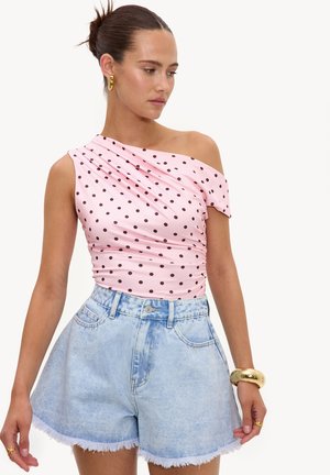 Kvinde iført en pink, asymmetrisk polkaprikket top og lyseblå, højttaljede denimshorts med frynser.