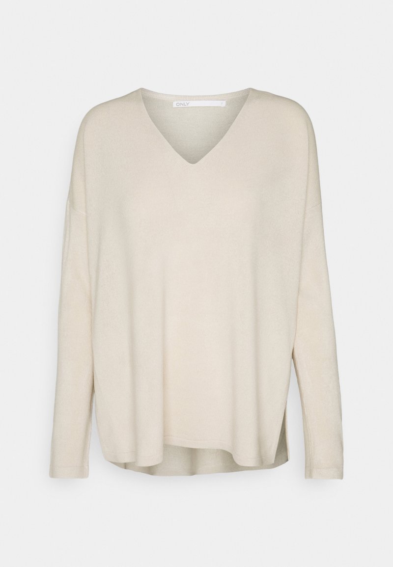 Pull beige à manches longues avec encolure en V, coupe ample et ourlet arrière légèrement plus long, présenté sur un fond gris clair uni.