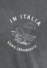 La tela de algodón gris presenta un gráfico blanco de una tumbona con una sombrilla y el texto "EN ITALIA SONO INNAMORATO" en un diseño circular.