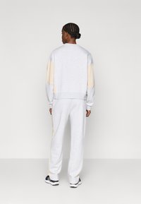 Γκρι σετ φούτμπολ και παντελόνι με ανοιχτού μπεζ λεπτομέρειες, κατασκευασμένο από μαλακό υλικό. Διαθέτει ριμπ τελείωμα και χαλαρή εφαρμογή.