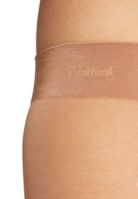 Collant trasparenti color sabbia con una texture liscia, una cintura elastica ampia e un branding discreto sulla banda. Il tessuto è leggero e lucido.