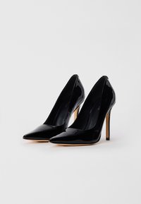 Mustad lakknahast kõrged kontsakingad, millel on teravad varbad, peensulged stiletto-kontsud ja sile, läikiv pind. Omaduseks on minimalistlik disain.