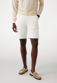 Hvide cargo shorts med to sidelommer, lavet af letvægtsstof. Sammen med beige loafers og en lyse beige langærmet skjorte.