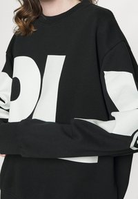 Sudadera negra con grandes letras gráficas blancas, con mangas blancas contrastantes y puños acanalados. Fabricada con un material suave y texturizado.