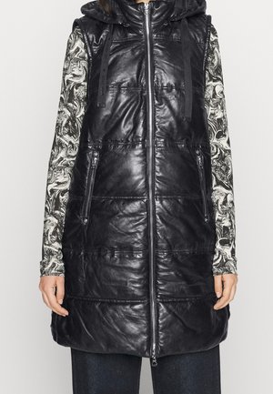 Veste sans manches matelassée noire brillante avec capuche, fermeture éclair devant et poches zippées portée sur un haut à manches longues à motif noir et blanc.