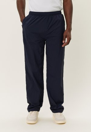 Pantaloni blu navy con elastico in vita, dal tessuto leggero e liscio, caratterizzati da un fit morbido e tasche laterali, abbinati a sneakers chiare.