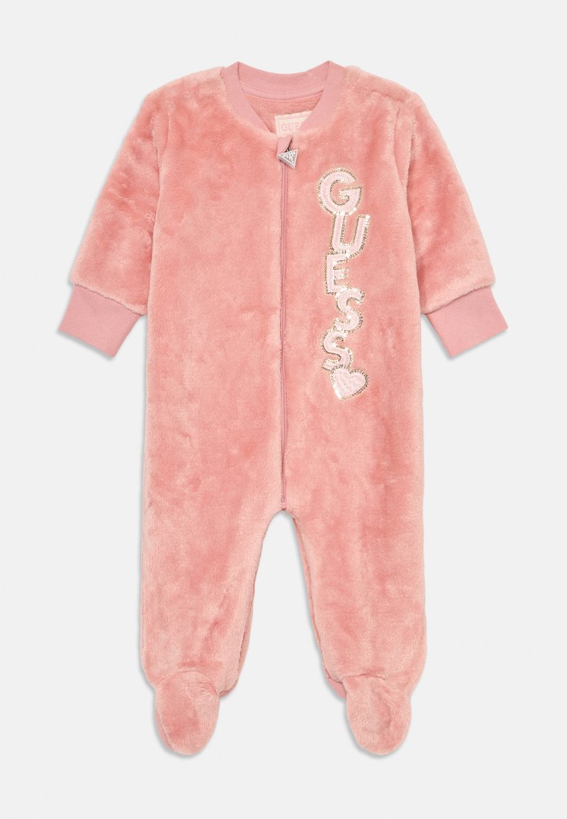 Combinaison en peluche douce rose pour bébé avec des manches longues, des jambes pieds, une fermeture éclair à l'avant et un logo "GUESS" vertical avec des sequins et un détail en cœur.