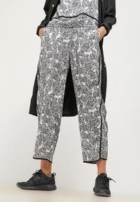Pantalon noir et blanc à motifs avec un design de feuilles, longueur cropped, taille élastique et poches latérales ; assorti à des chaussures noires.