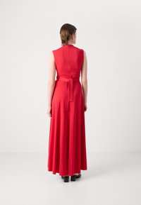 Robe maxi sans manches rouge avec un corsage ajusté, taille ceinturée et jupe fluide. Texture lisse, couleur unie et fermeture éclair au dos.