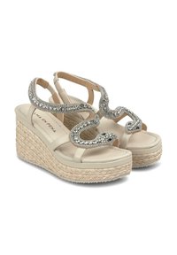 Sandales compensées beige avec une plateforme en jute tressé, présentant un accent décoratif en cristal en motif ondulé sur les brides.