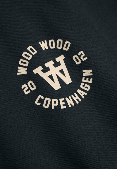 Tissu noir avec un logo circulaire en crème, le texte comprend "WOOD WOOD", "COPENHAGUE" et l'année "2002", avec un "W" stylisé.