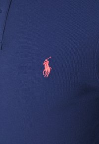 Blue textured fabric with small embroidered pink logo of a polo player on horseback holding a raised mallet.