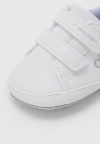 Bela otroška čevljica iz gladkega sintetičnega materiala, z ježki, okroglim sprednjim delom in srebrnim logotipom.