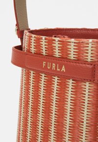 Czerwona i beżowa pleciona torebka z paskiem ze skóry i złotym logo „FURLA” na skórzanej naszywce w pobliżu górnej krawędzi.
