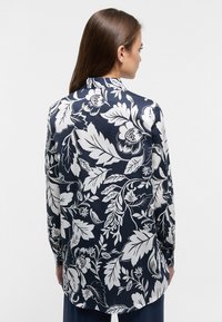 Navy blue long-sleeve shirt with a floral white pattern, featuring a classic collar and curved hem, made of smooth fabric.