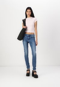 Lys rosa cropped t-skjorte, tettsittende, kombinert med blå denim skinny jeans. Sorte platåhæler og en svart totebag er også synlige.