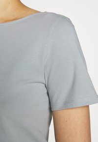 Nærbillede af en person iført en lyseblå kortærmet skjorte, der viser skulderen, ærmet og området over brystet.