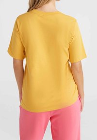 Camiseta amarilla de algodón con mangas cortas y cuello redondo, combinada con pantalones rosa claro, que muestra una textura suave y un ajuste relajado.