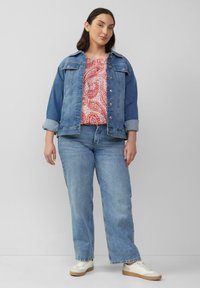 Lichtblauwe denimjack over een rood paisleypatroon top, gecombineerd met lichte jeans en beige sneakers. Eenvoudig ontwerp en casual pasvorm.