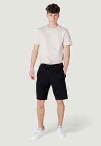 Men's casual outfit featuring a light beige cotton t-shirt and black drawstring shorts, paired with white sneakers. Simple design, relaxed fit.