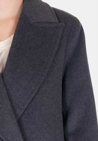 Cappotto grigio in lana con colletto a scollatura, texture morbida e vestibilità sartoriale. Caratterizzato da un design pulito e dettagli di cucitura precisi.