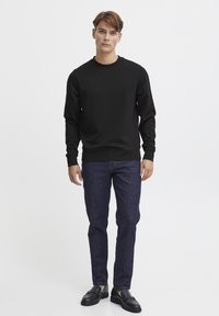 Black sweatshirt with round neck, long sleeves, and ribbed cuffs, paired with dark blue jeans and black loafers, set against a white background.