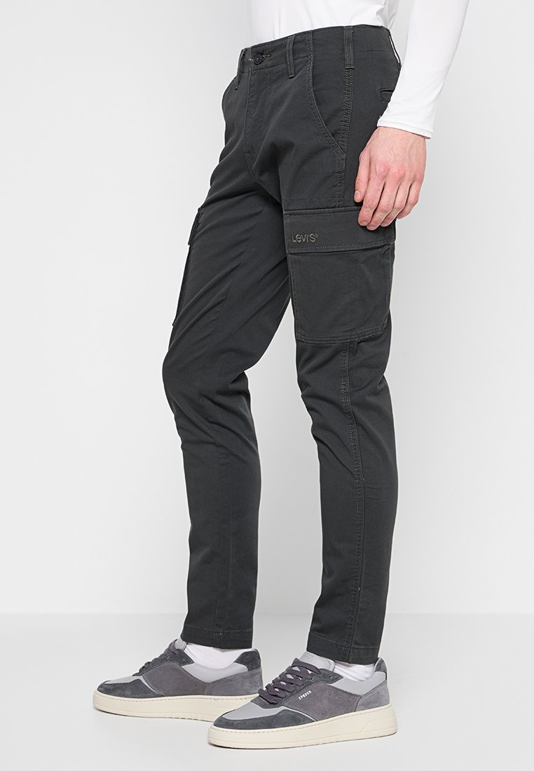 Pantalones cargo negros con corte ajustado, que cuentan con múltiples bolsillos, cremallera en la bragueta y detalles de costura. Fabricados con tejido duradero.