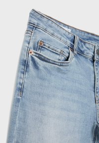 Ljusblå denimjeans i närbild som visar framficka, mindre myntficka, bältesögla, kopparnit och kontrastsöm på slätt tyg.