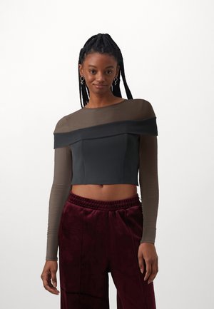 Un crop top noir ajusté, avec des manches longues en tissu transparent marron et un design décolleté ; associé à un pantalon en velours bordeaux.