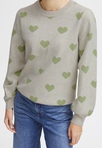 Pull gris clair avec des motifs en forme de cœur verts, col rond côtelé et manches longues, assorti avec un jean en denim bleu.
