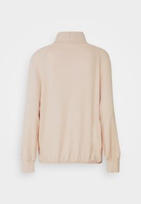 Sweatshirt rose clair avec un col montant, des poignets côtelés et une coupe décontractée. Le tissu semble doux avec une texture lisse.