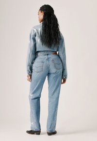 Lichtblauwe denimjas en jeans met een pasvormontwerp, versierd met witte ornamentale patronen langs de broekspijpen en zilveren studs op de jas.