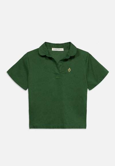 Πράσινο σκούρο κοντομάνικο πόλο με μικρό κίτρινο γεωμετρικό λογότυπο στο αριστερό στήθος και στρογγυλεμένο γιακά.